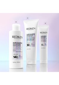 Trzy butelki koncentratu do włosów Redken Acidic Bonding w różnych rozmiarach na pastelowym tle.