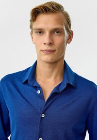 Blauwe overhemden gemaakt van een zachte stof; heeft een kraag, lange mouwen en contrasterende witte knopen; gladde textuur met subtiele glans.