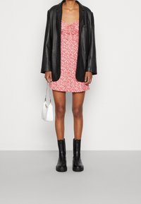 Czerwona sukienka w kwiaty z dopasowanym gorsetem i rozszerzanym dołem, założona pod czarną skórzaną marynarkę. Połączona z czarnymi botkami za kostkę i białą torebką.