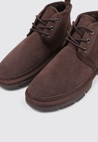 Botines de ante marrón con punta redonda y cordones. Parte superior texturizada y cuello acolchado en el tobillo. Suela de goma con tracción.