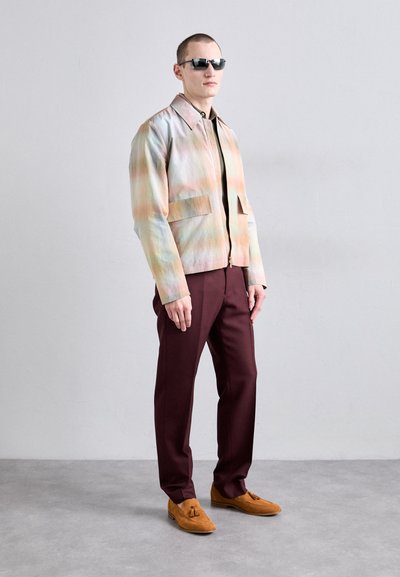 Multicolored jacket with a gradient pattern, two front pockets, paired with maroon trousers and brown suede loafers. Sunglasses complete the look.