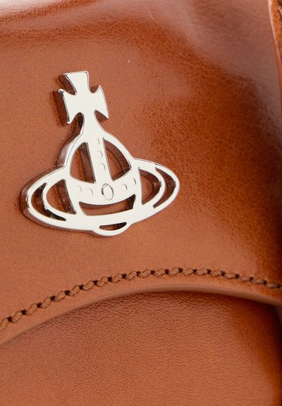 Superficie in pelle marrone con un bordo cucito; presenta un logo argentato lucido che somiglia a un globo con una croce sopra.