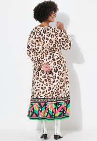 Leopardprint lang kjole med en mønstrede flerfarvet kant, der har lange ærmer og en indsnævret talje, parret med sølvfarvede ankelstøvler.