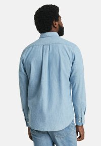 Lys blå chambray skjorte med lange ærmer og knap-ned krave, med en rygfald og rundet kant. Polyester materiale, afslappet design.