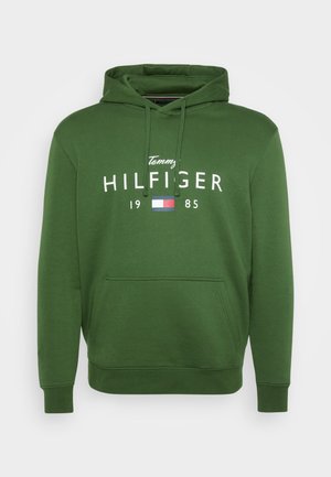 Sweatshirt verde com uma textura suave, apresentando um bolso canguru, capuz ajustável e texto branco "Tommy HILFIGER 1985" com um destaque em bandeira colorida.