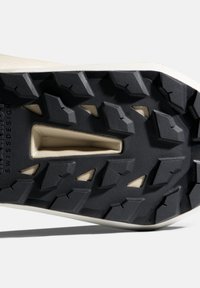 Κοντινή λήψη μαύρης και μπεζ ανθεκτικής σόλας παπουτσιού με βαθιά αυλάκια και κείμενο "SWISSDESIGN" σε υφασμένη επιφάνεια καουτσούκ.