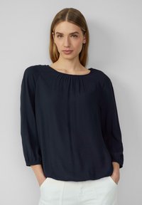 Dunkelblaue Bluse mit einem runden Ausschnitt, Dreiviertelärmeln und Raffung an den Schultern, aus einem leichten Stoff gefertigt.