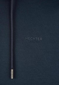 Navyblauwe ritssluiting hoodie met een gladde textuur, voorzien van een reliëflogo "HECHTER PARIS" en een metallic ritssluiting als accent.