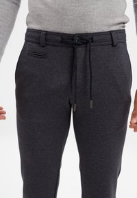 Ciemnoszare spodnie dresowe z teksturowanej tkaniny, z уздą w pasie, regulowanym pasem i bocznymi kieszeniami, zapewniające swobodny krój.