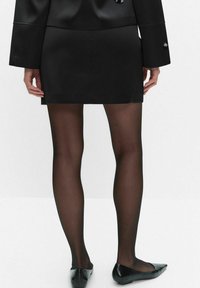 Czarna mini spódnica w połączeniu z przezroczystymi czarnymi rajstopami i czarnymi balerinami; gładki materiał z minimalnymi detalami i dopasowanym krojem.
