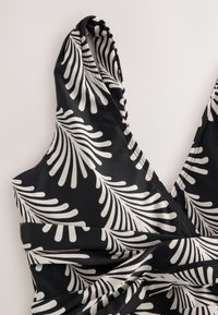 Vêtement noir sans manches avec des motifs abstraits blancs en forme de feuilles et un décolleté profond en V avec un tissu froncé à la taille.