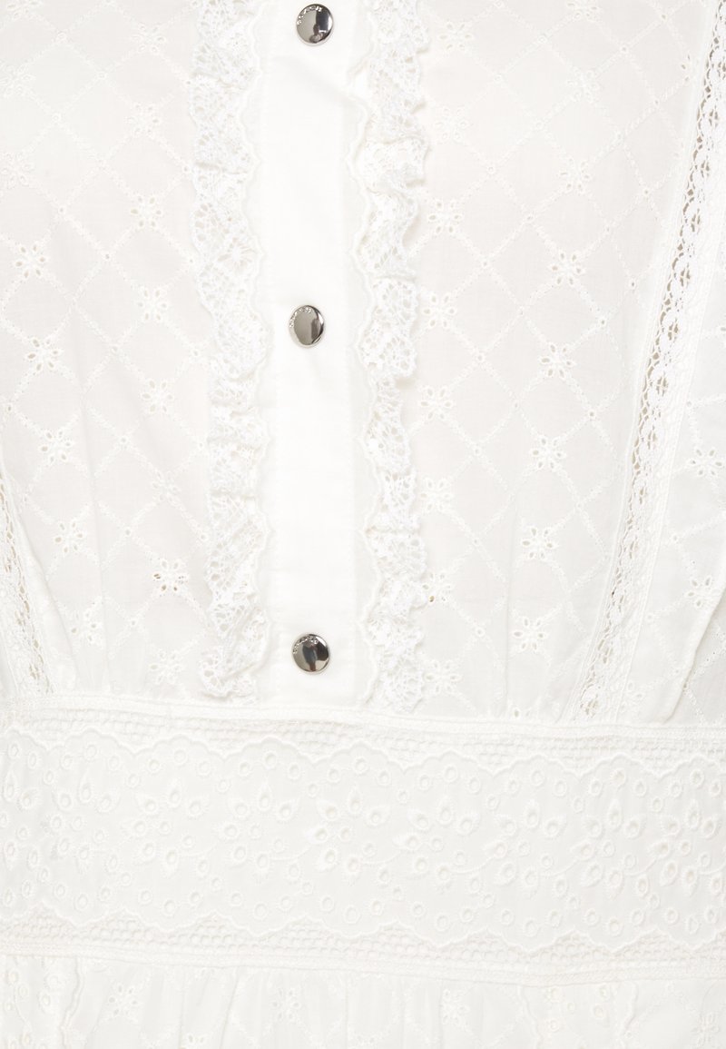 Weißes Kleid aus strukturiertem Baumwollstoff mit Rautenmustern, Spitzenbesatz und dekorativen Knöpfen auf der Vorderseite. Gemusterter Taillengürtel.