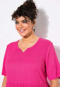 Fuksiavaate, jossa on teksturoitu kangas, V-pääntie, lyhyet hihat ja rento malli. Kevyt ja rento muotoilu.