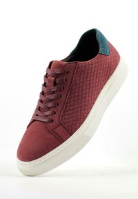 Rode suède sneakers met geweven textuur, platte witte rubberen zool en blauwe suède accenten bij de hak. Voorzien van veters en gestikte details.