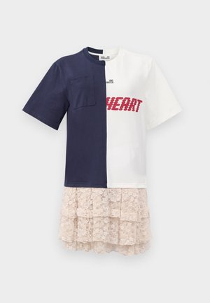Camiseta de algodón mitad azul marino, mitad blanca, con un bolsillo de parche, bordado "CORAZÓN" en rojo, y una falda de encaje en capas de color beige claro.