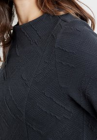 Abito nero con texture caratterizzato da scollatura rotonda e un intricato motivo che evidenzia una superficie texturizzata in rilievo con un aspetto ondulato.