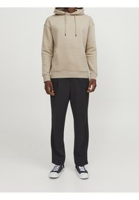 Sudadera beige con bolsillo canguro, capucha ajustable con cordón y dobladillo acanalado. Combinada con pantalones negros de corte ajustado y zapatos negros.