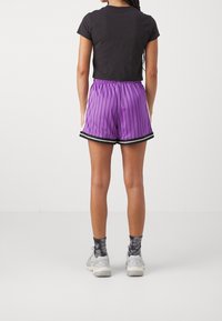 Fialové pruhované sportovní šortky s černými akcenty, doplněné přiléhavým černým tričkem a šedými teniskami, pohled zezadu.