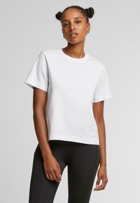 T-shirt en coton blanc à manches courtes et col rond. Porté avec des leggings noirs, dotés d'une coupe décontractée et d'une texture lisse.