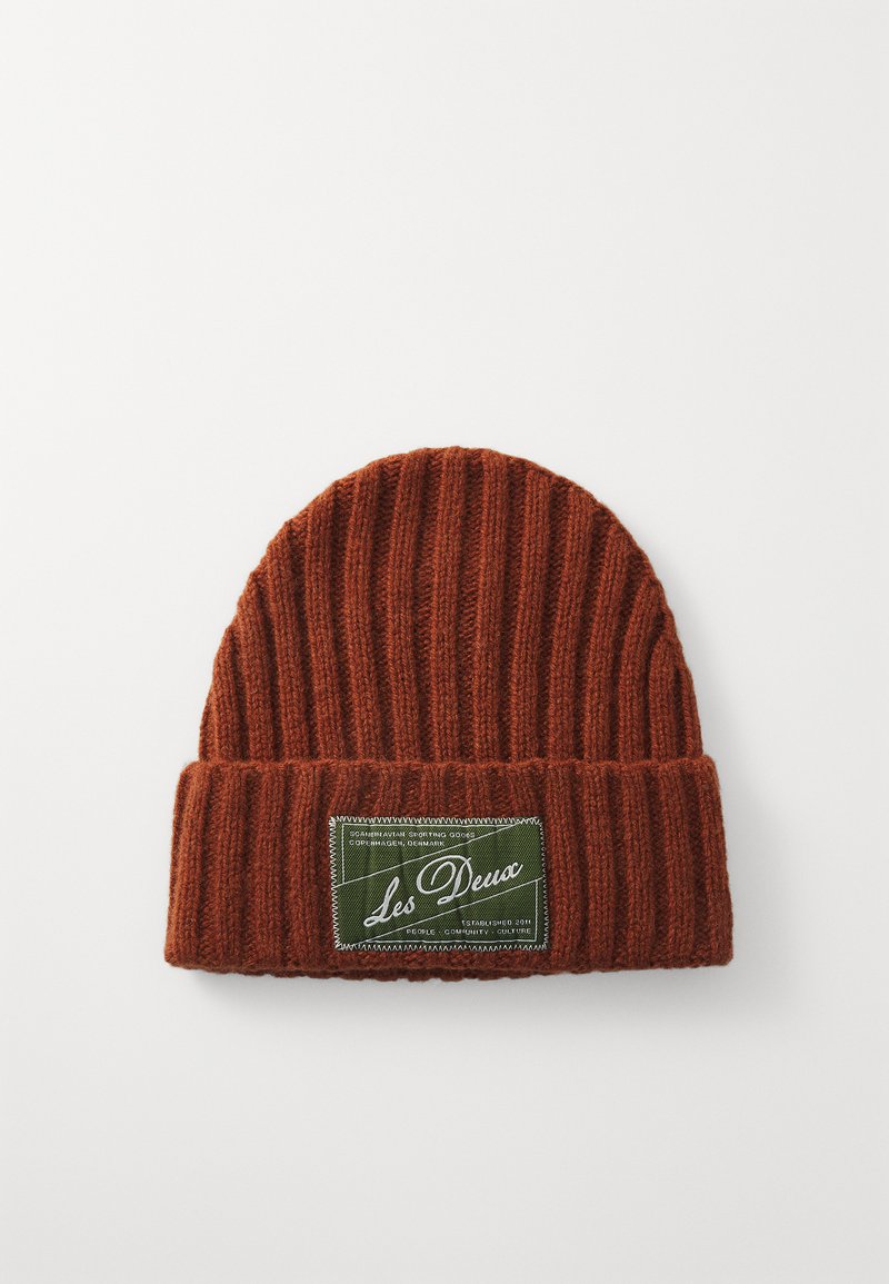 Ribbede strikkede beanie i rustrød, med en foldet kant og et grønt logo-patch med hvid tekst, lavet af behageligt stof for varme.