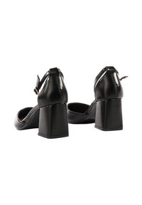 Scarpe in ecopelle nera con tacco a blocco, punta rotonda, cinturino alla caviglia e texture liscia; la vista da dietro mostra un design robusto del tacco.