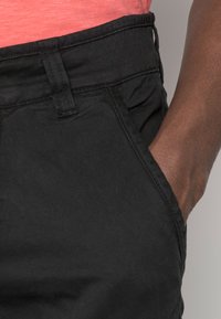 Černé bavlněné kalhoty s hladkou texturou a klasickým střihem, s běžným pasem a bočními kapsami.