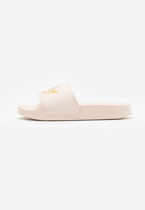 Beigenvärinen Adidas-liukusandaali, jossa leveä hihna, jossa on vaaleanruskea Adidas-trefoil-logo, ja litteä pohja.
