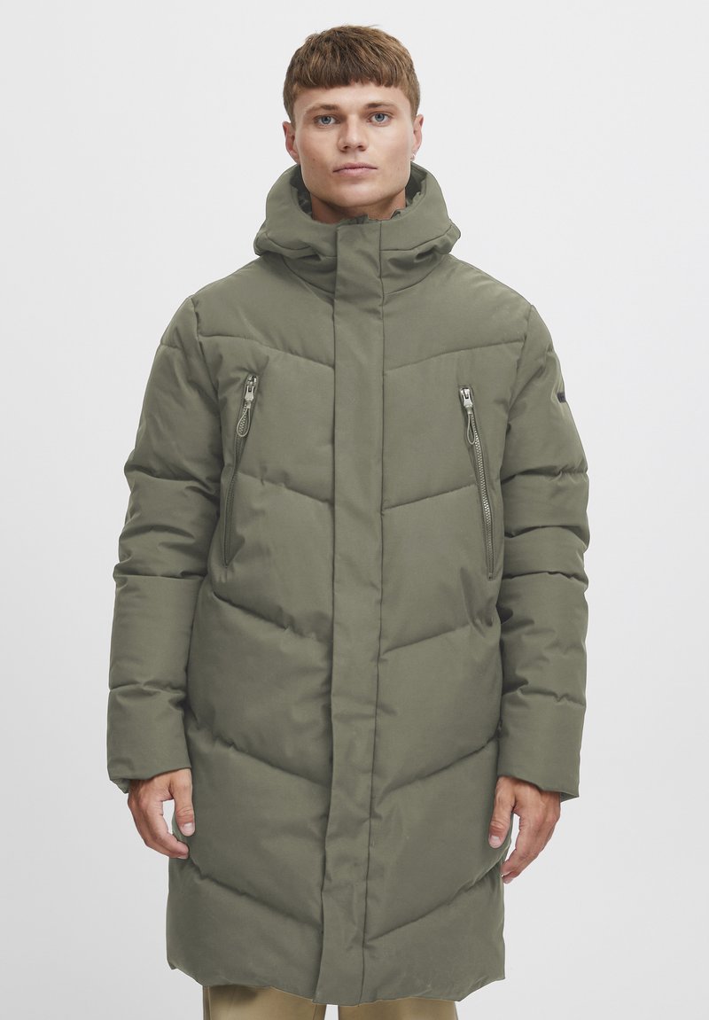 Polstret parka i olivengrønn med høy krage, glidelåslommer foran og lang design. Glatt tekstur og horisontale quiltedetaljer.