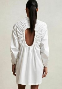 Rochie albă, cu mâneci lungi, prezentând un spate plisat cu o decupare ovală mare.Țesătură netedă, croi lejer, design de lungime până la genunchi.