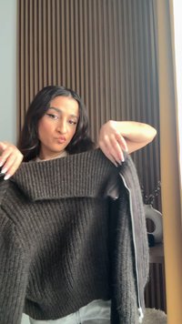 Maglione marrone a coste con un ampio colletto e dettaglio con cerniera sul lato sinistro, che mostra un motivo lavorato a maglia strutturato.