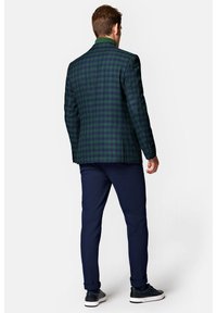 Kostium w kolorze ciemnozielonym i granatowym w kratę o uporządkowanej formie. Zestawiony z granatowymi spodniami o gładkim wykończeniu oraz sneakersami.
