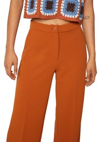 Rostfärgade vida byxor i ett mjukt tyg, med en knäppning fram och rena linjer som framhäver en skräddarsydd passform.