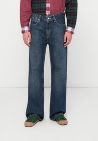 Jeans in denim blu scuro con vestibilità a gamba larga, caratterizzati da un classico design a cinque tasche e hardware in metallo. Tessuto testurizzato con lieve sbiadimento.