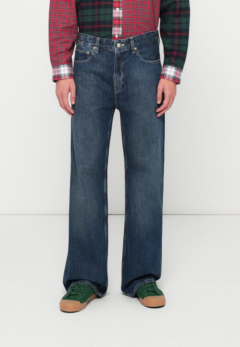 Jeans in denim blu scuro con vestibilità a gamba larga, caratterizzati da un classico design a cinque tasche e hardware in metallo. Tessuto testurizzato con lieve sbiadimento.