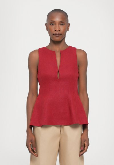 Haut peplum rouge avec encolure en trou de serrure et design sans manches, fabriqué en tissu texturé. Associé à un pantalon beige taille haute.