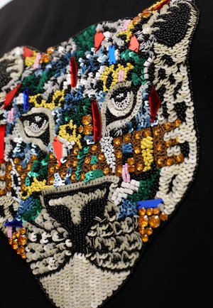 Textil negro bordado con un diseño colorido de tigre hecho de lentejuelas, cuentas y hilos texturizados, que muestra detalles y patrones intrincados.