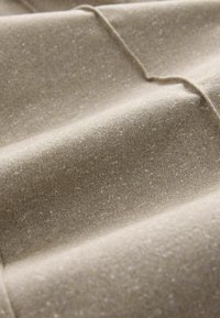 Textuur, zandbeige stof met een subtiele glans. Kenmerkt zich door zachte, golvende plooien en fijne, korrelige details.