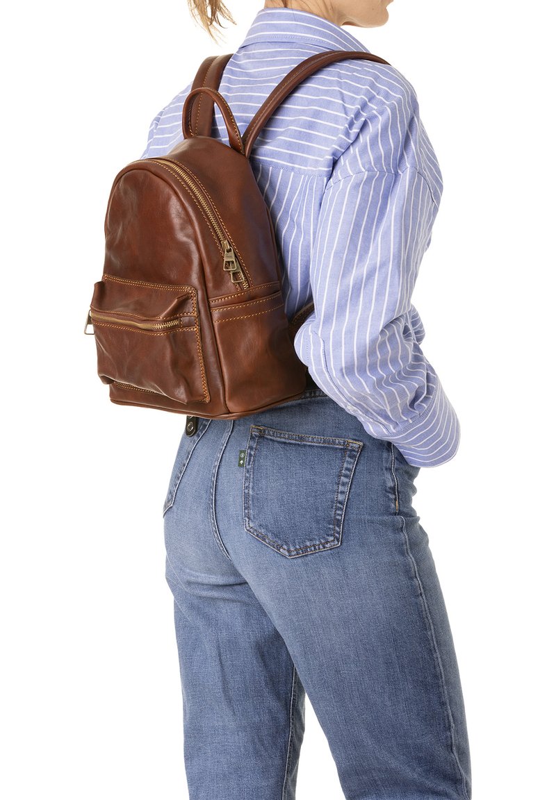 Sac à dos en cuir marron de forme arrondie, avec une poche avant et des fermetures éclair dorées. Bretelles ajustables et texture lisse.