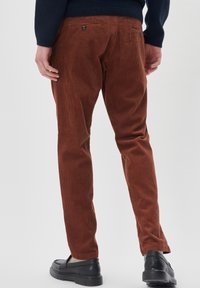 Pantaloni din corduroy maro, cu dungi verticale, design slim fit, două buzunare la spate cu nasturi și pantofi negri slip-on.