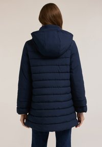 Chaqueta acolchada azul marino con capucha, diseño acolchado con costuras horizontales y mangas largas, mostrada desde atrás.