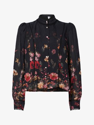 Blouse noire à motifs floraux en tissu texturé. Elle présente un col haut, des manches longues avec des poignets boutonnés et une garniture en dentelle décorative sur le devant.