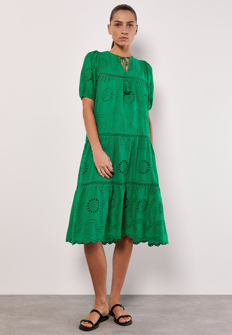 Grünse Baumwollkleid mit kurzen Puffärmeln, bestickten Details und einem gestuften Rock. Besitzt einen runden Halsausschnitt und einen Spitzenbesatz am Saum.