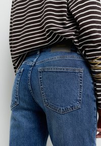 Hochgeschnittene blaue Denim-Jeans mit glatter Textur, auffällig genähten Nähten und Gesäßtaschen. Mit einem schwarzen "PULL&BEAR"-Label versehen.