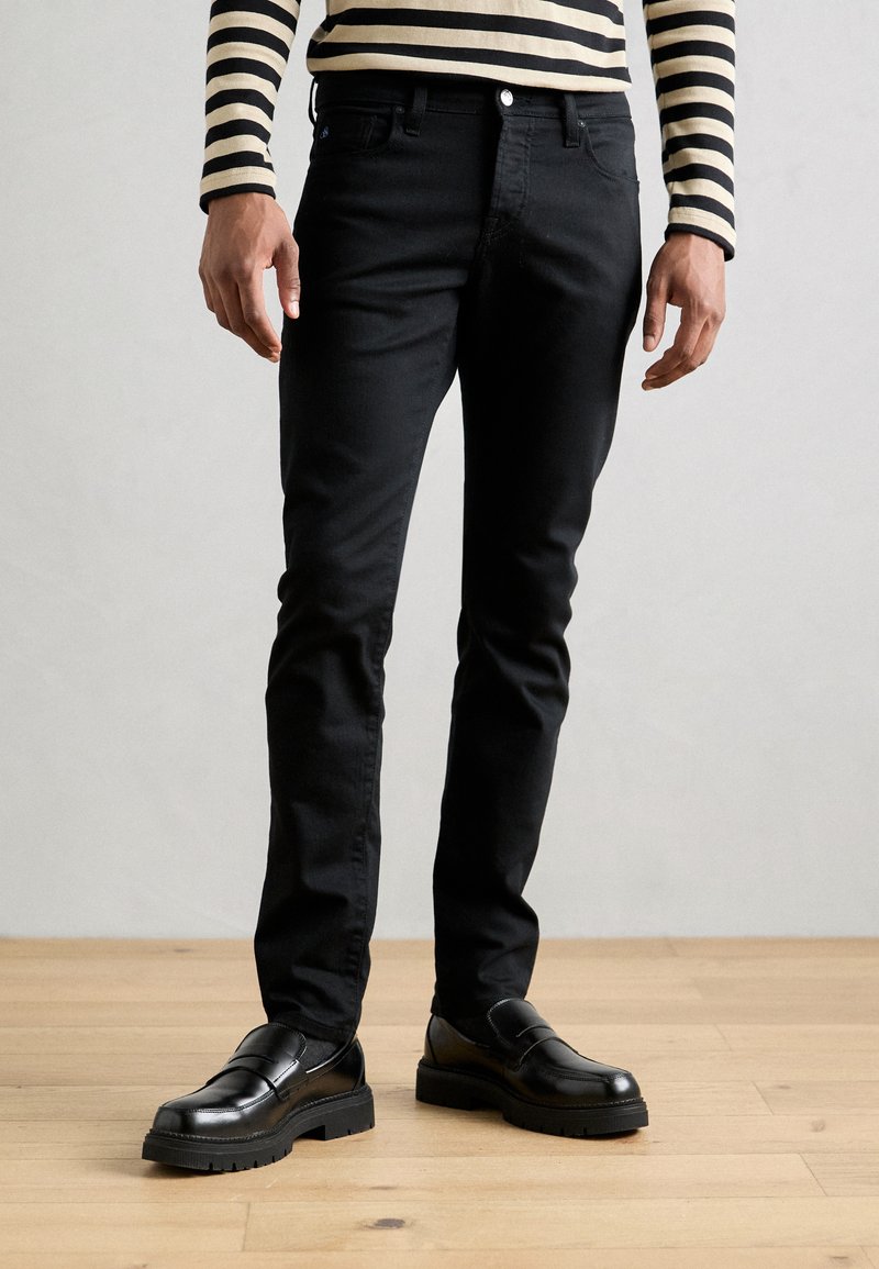 Sorte denimbukser har en slim fit og fem-lommers design. Kombinert med sorte lær slip-on sko, begge med teksturerte såler.