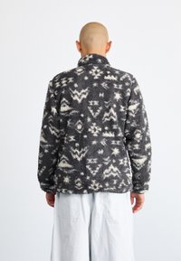Grau- und cremefarbener Fleecejacke mit Muster, hohem Kragen, weicher Textur und lockerer Passform. Verfügt über abstrakte, geometrische Designs.