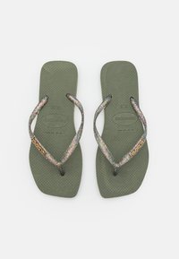 Chinelos verde-oliva com solas texturizadas, apresentando tiras brilhantes e iridescentes e um detalhe em logo dourado numa das tiras.