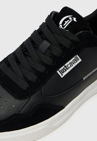 Mustad sneaker paksude kudumislintidega, valge "Just Cavalli" logo küljes ja valge tallaõmblusega.