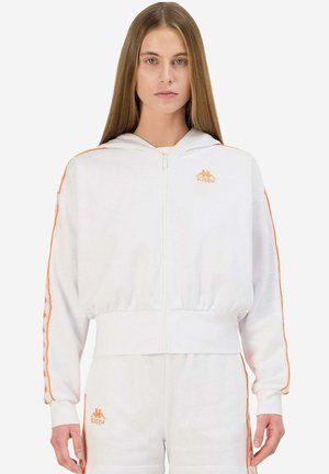Sudadera blanca con cremallera y detalles en naranja, incluyendo un logo. Presenta capucha, cinturilla elástica y franjas laterales con una marca repetida. Material suave.