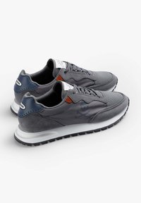Graue Sportschuhe, die eine Mischung aus strukturierten Materialien, eine weiße Sohle und ein kleines Totenkopf- und Kreuzbones-Detail an der Seite aufweisen.