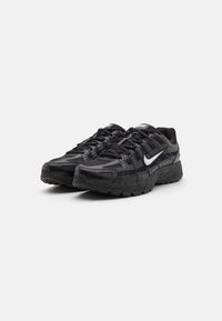 Baskets de sport noires avec une tige en mesh, un design texturé et une semelle en caoutchouc. Présente un logo Nike en swoosh blanc bien visible.